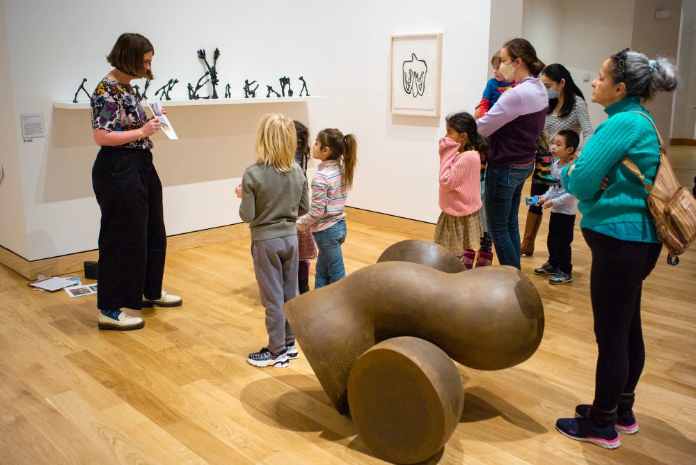 Several adults and children in a gallery looking at a drawing while surrounded by art.